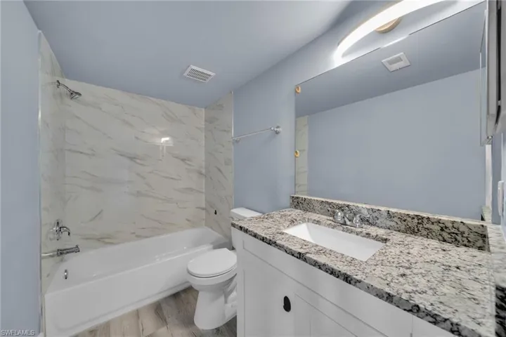 Bathroom featuring a white vanity with a light-toned granite countertop, an undermount sink, and a large wall-mounted mirror