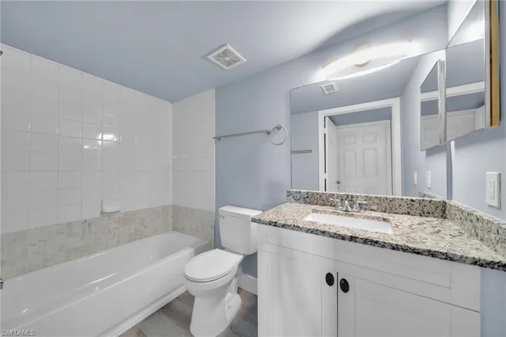 Bathroom featuring a white bathtub, a tiled shower surround with a decorative accent band, a white toilet, a vanity with a white cabinet, and a speckled countertop