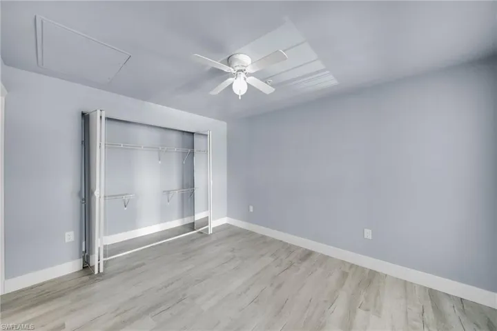Room featuring wood-finish flooring, light blue wall paint, white baseboards, and a ceiling fan with integrated lighting