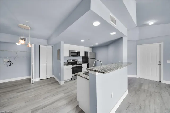 Open-concept kitchen and living area featuring wood-finish flooring, white cabinetry, and stainless steel appliances