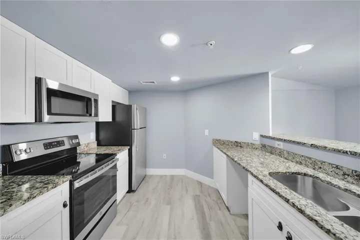 Modern kitchen featuring stainless steel appliances, white cabinetry, speckled countertops, wood-finish flooring, and recessed lighting