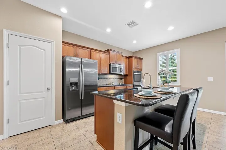 Kitchen with dark stone counters, light tile flooring, stainless steel appliances, backsplash, and a kitchen island with sink