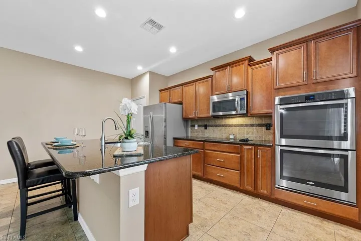 Kitchen featuring dark stone countertops, appliances with stainless steel finishes, a kitchen island with sink, tasteful backsplash, and light tile flooring