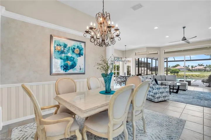 Tiled dining space with ceiling fan with notable chandelier and ornamental molding