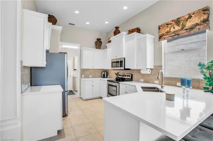 Kitchen with sink, kitchen peninsula, white cabinetry, appliances with stainless steel finishes, and a breakfast bar area