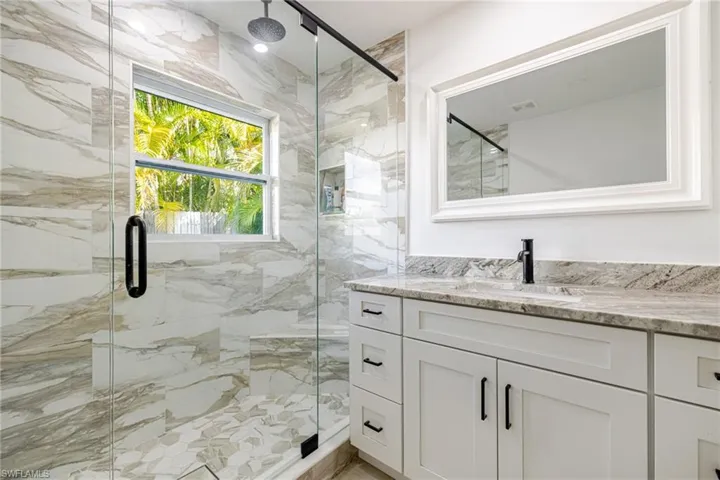 Full bath featuring a marble finish shower and vanity