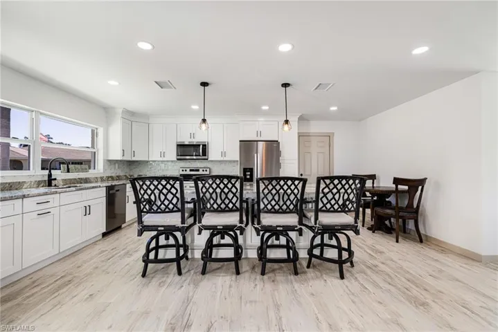 Kitchen with hanging light fixtures, white cabinetry, recessed lighting, stainless steel appliances, and light stone counters