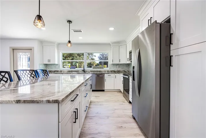 Kitchen with stainless steel appliances, light wood-style floors, light stone counters, white cabinetry, and recessed lighting