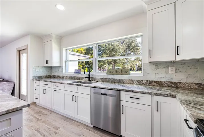 Kitchen with dishwasher, white cabinets, light wood finished floors, backsplash, and light stone countertops