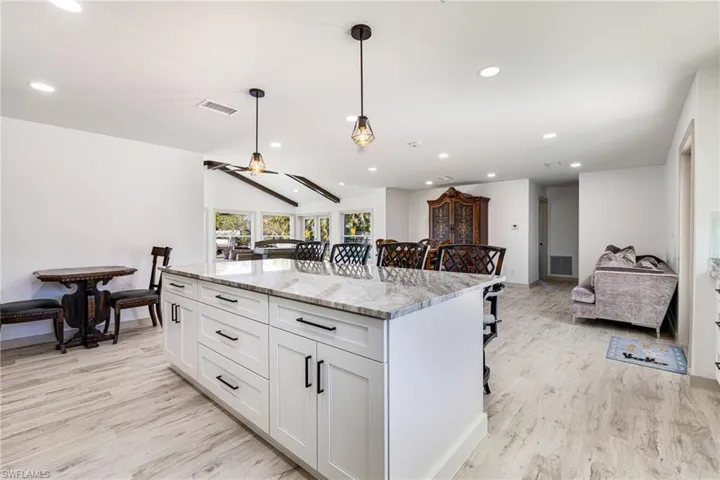Kitchen featuring a kitchen bar, light stone counters, a kitchen island, open floor plan, and vaulted ceiling