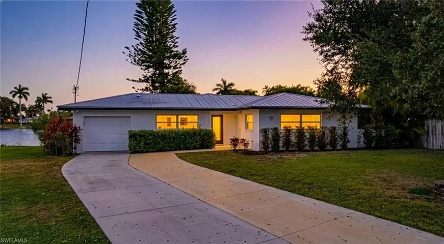 View of front of house featuring a garage, a metal roof, concrete driveway, and a front lawn