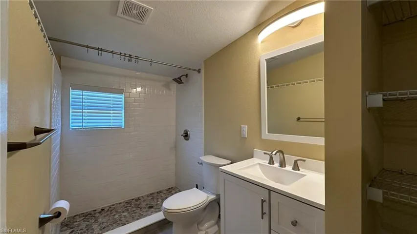 Bathroom featuring vanity, lofted ceiling, toilet, a textured ceiling, and a tile shower