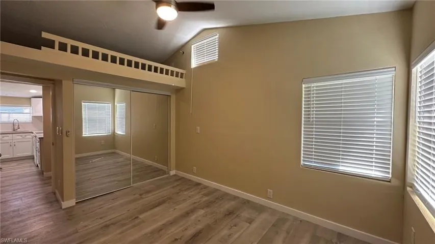 Unfurnished bedroom featuring ceiling fan, a closet, hardwood / wood-style floors, and lofted ceiling