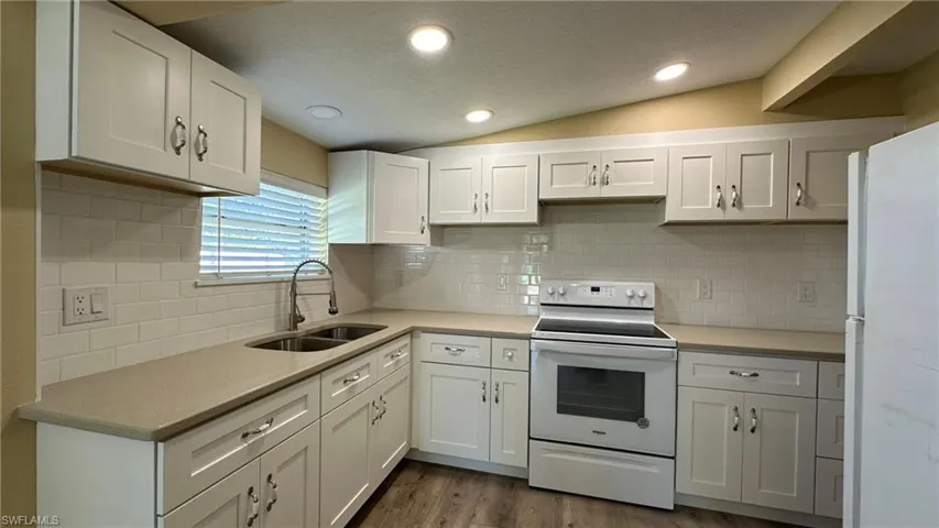 Kitchen featuring white cabinets, lofted ceiling, electric stove, and sink