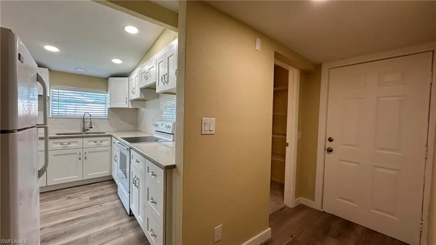 Kitchen featuring white cabinetry, sink, light hardwood / wood-style flooring, white appliances, and decorative backsplash