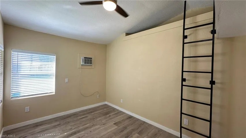 Spare room with hardwood / wood-style floors, lofted ceiling, an AC wall unit, ceiling fan, and a textured ceiling