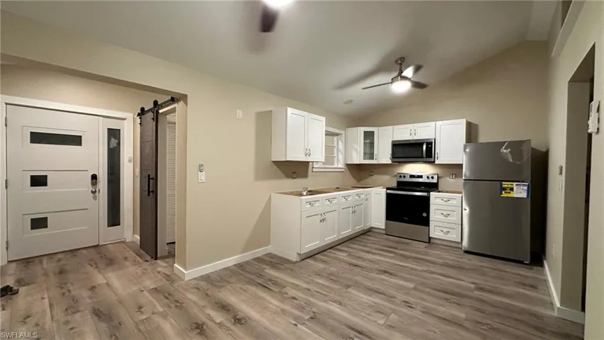 Kitchen with white cabinets, vaulted ceiling, a barn door, light wood-type flooring, and appliances with stainless steel finishes