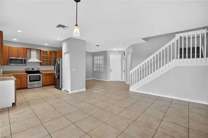 Open-concept living area with large format tile flooring, a kitchen featuring wood cabinetry and stainless steel appliances, a white staircase with balusters, and recessed lighting