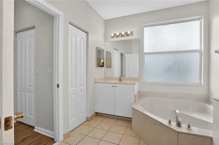 Bathroom featuring a corner soaking tub with deck-mounted fixtures, a single vanity with base cabinetry, and a mirrored medicine cabinet