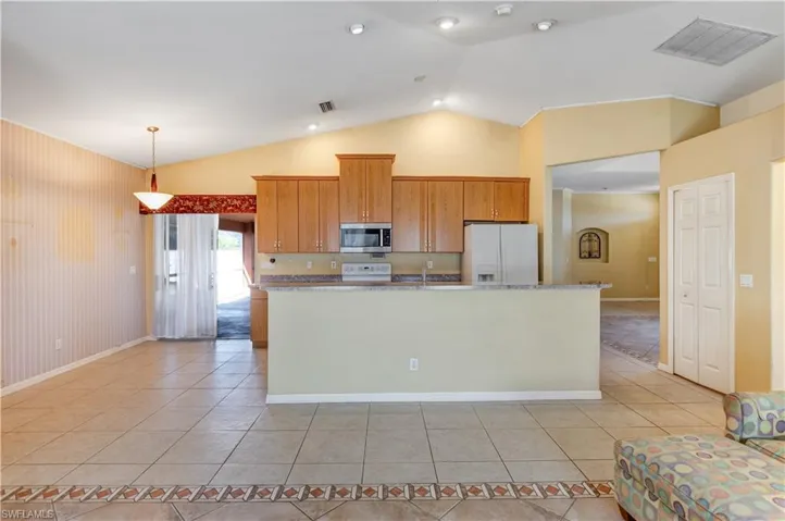 Kitchen with white appliances, pendant lighting, light tile patterned floors, wood finish cabinetry, and a kitchen island with sink