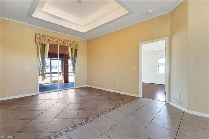 Empty room with a raised ceiling, ornamental molding, tile patterned flooring, and healthy amount of natural light