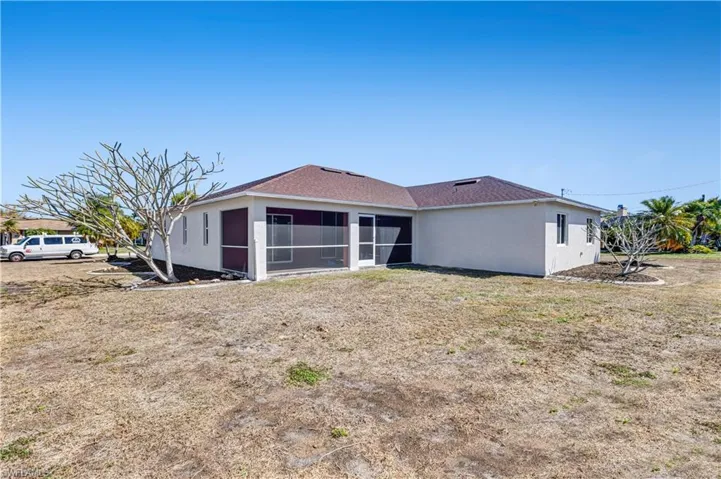 Back of property featuring a sunroom, stucco siding, and a lawn