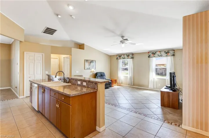 Kitchen featuring light tile patterned floors, a kitchen island with sink, wood finish cabinets, ceiling fan, and open floor plan