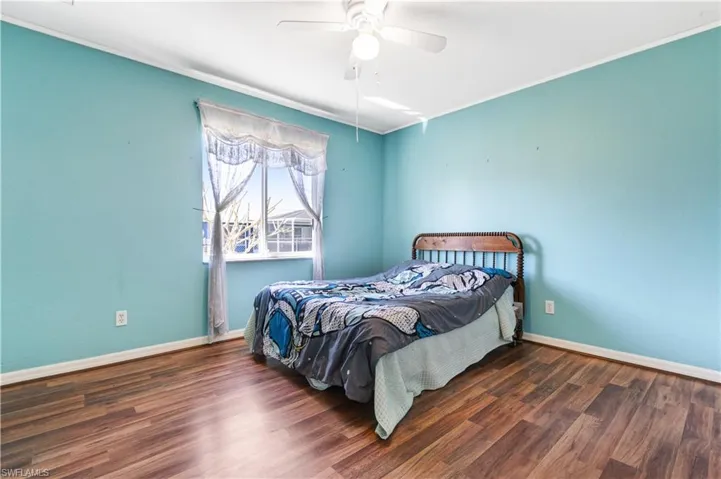 Bedroom with dark wood-style floors, a ceiling fan, and ornamental molding