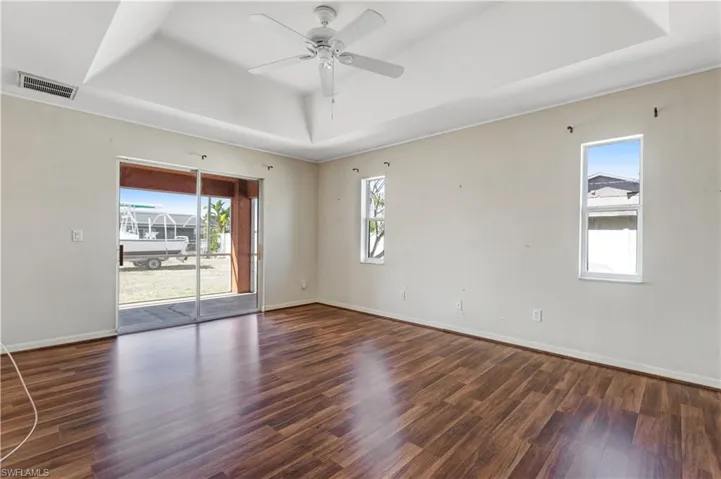 Empty room with ceiling fan, a raised ceiling, plenty of natural light, and dark wood finished floors