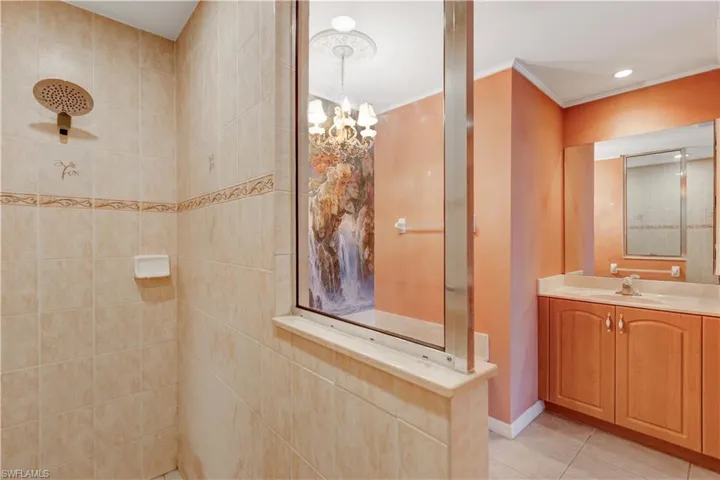 Full bathroom with vanity, a tile shower, light tile patterned floors, crown molding, and hanging lights