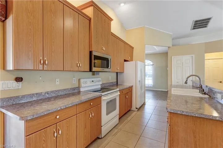 Kitchen featuring white appliances, light tile patterned flooring, wood finish cabinetry, and a center island with sink