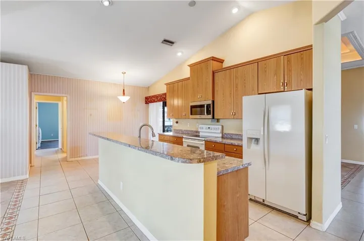 Kitchen with white appliances, light tile patterned flooring, decorative light fixtures, vaulted ceiling, and wood finish cabinetry