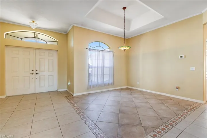 Entryway featuring ornamental molding, light tile patterned flooring, inlaid floor details, and a tray ceiling