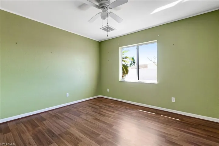 Empty room with dark wood-style floors, a ceiling fan, and ornamental molding