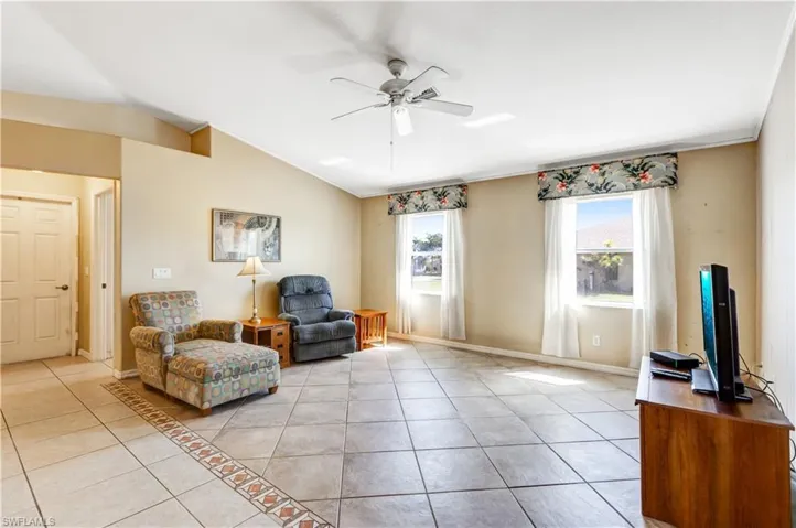Living area featuring light tile patterned flooring, ceiling fan, lofted ceiling, and crown molding