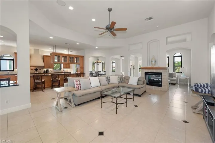 Living area with arched walkways, recessed lighting, a ceiling fan, light tile patterned floors, and a tiled fireplace