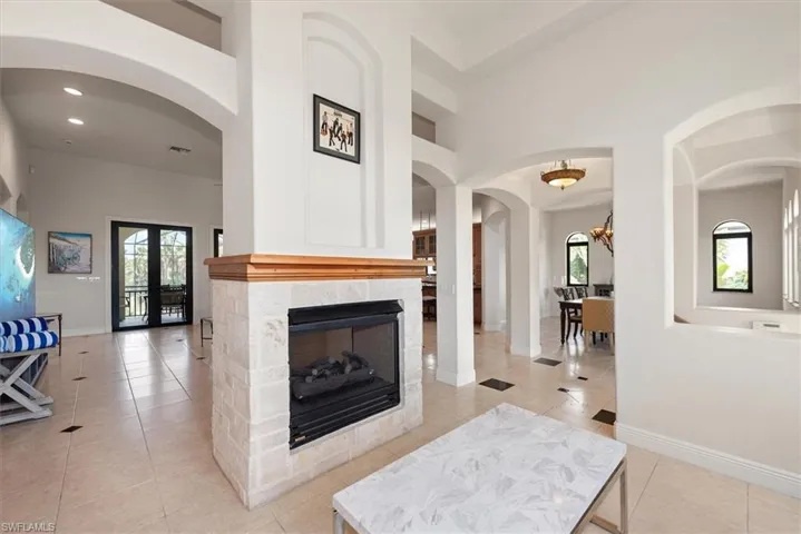 Living area with arched walkways, light tile patterned floors, a multi sided fireplace, a towering ceiling, and recessed lighting