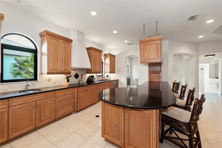 Kitchen with dark stone countertops, a kitchen breakfast bar, light tile patterned flooring, arched walkways, and decorative backsplash