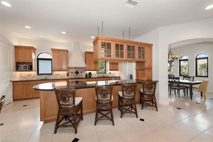 Kitchen featuring glass insert cabinets, light tile patterned floors, brown cabinetry, arched walkways, and recessed lighting