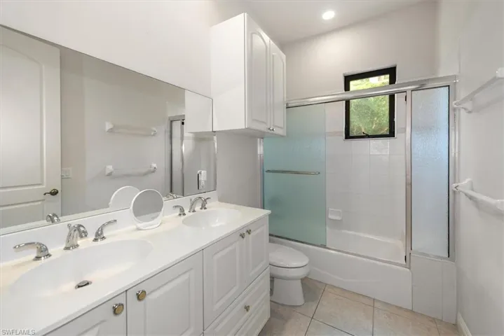 Full bath with combined bath / shower with glass door, double vanity, and light tile patterned flooring