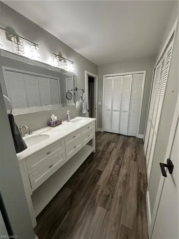 Full bath with a closet, double vanity, and dark wood finished floors