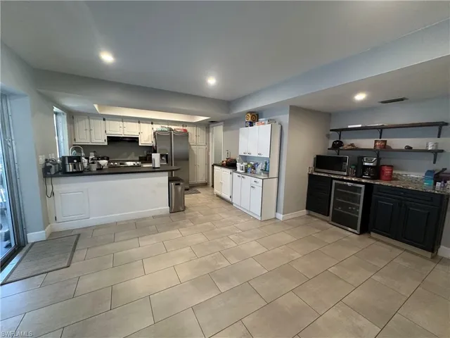 Kitchen featuring a peninsula, beverage cooler, appliances with stainless steel finishes, dark countertops, and white cabinets