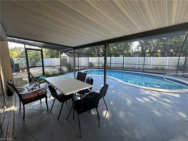 View of swimming pool featuring enclosure, a sunroom, a storage shed, and a fenced backyard