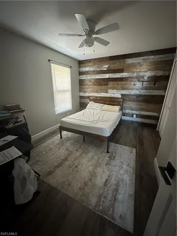Bedroom with dark wood finished floors, wood walls, and ceiling fan