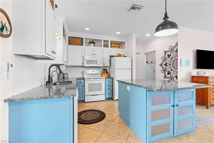 Kitchen with white appliances, blue cabinetry, light tile patterned floors, dark stone countertops, and pendant lighting