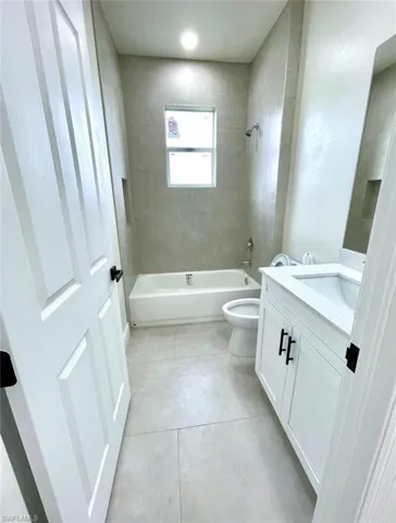 Full bathroom with toilet, tiled shower / bath combo, vanity, and tile patterned floors