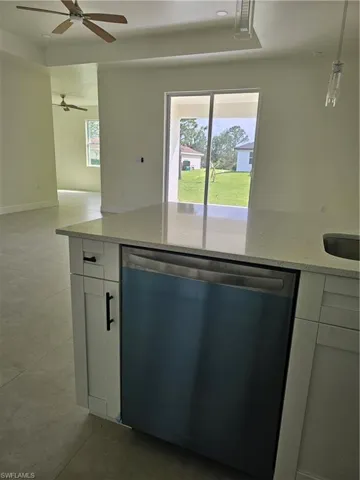 Kitchen featuring light stone countertops, ceiling fan, stainless steel dishwasher, white cabinets, and pendant lighting