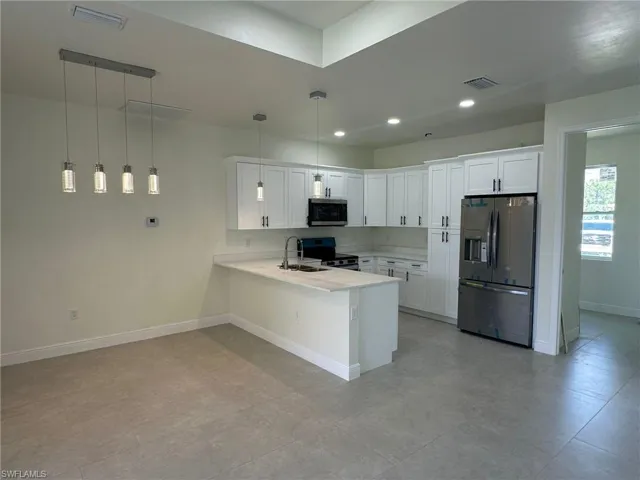 Kitchen with light tile patterned floors, hanging light fixtures, white cabinetry, stainless steel appliances, and kitchen peninsula