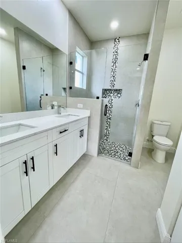 Bathroom featuring a shower with shower door, vanity, tile patterned floors, and toilet
