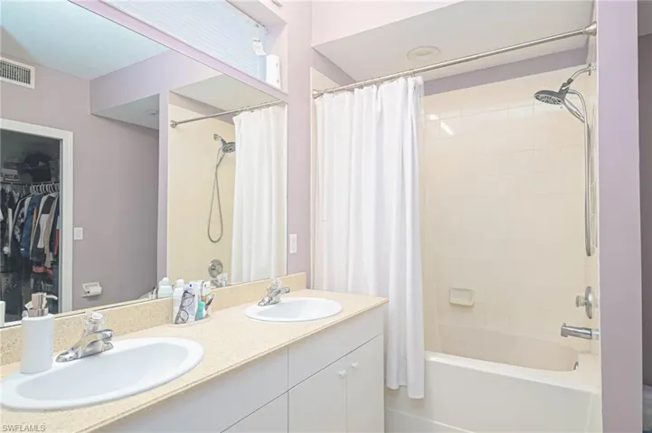 Full bathroom with shower / bath combination with curtain, double vanity, and a spacious closet